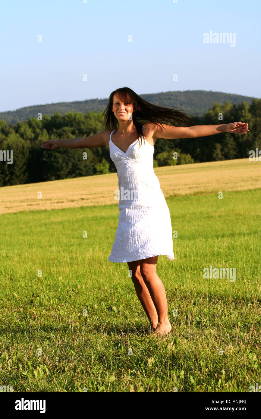 A young woman with long dark hair wearing a white dress stands barefoot ...