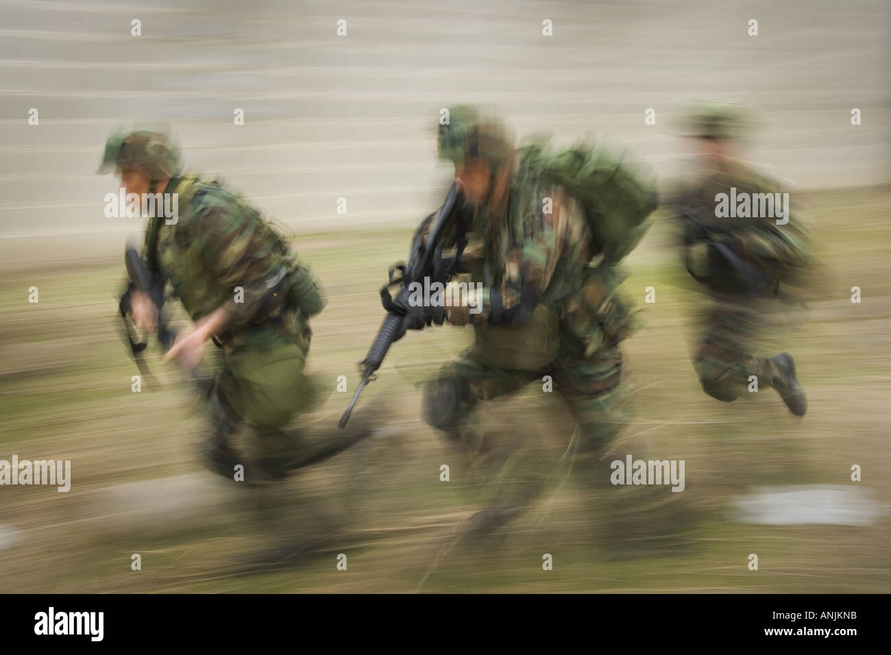 Three soldiers running on the field with their rifles Stock Photo