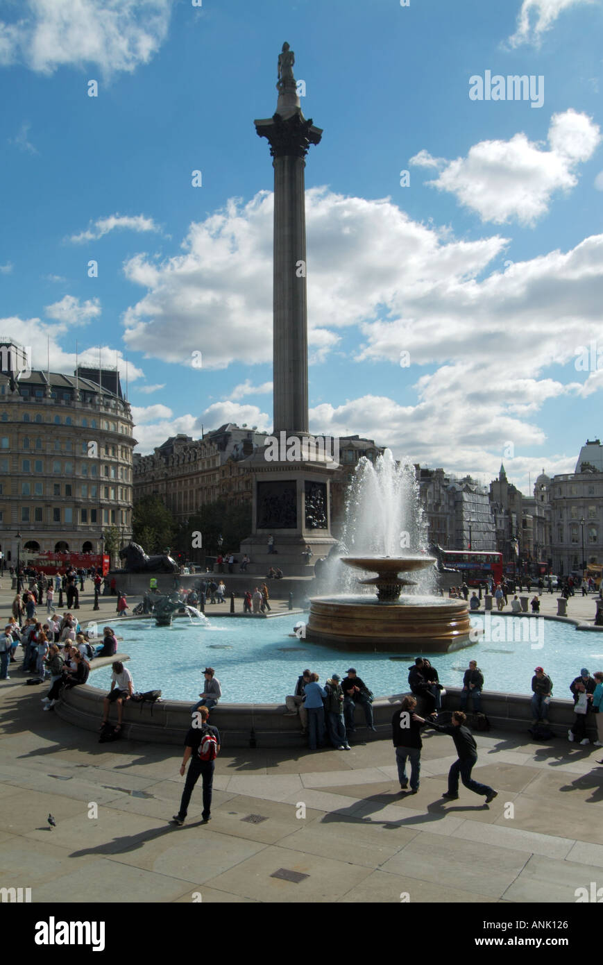 Tourists in Trafalgar Square historical landmark Nelsons Column with fountain water feature sunny blue sky day in London street scene England UK Stock Photo