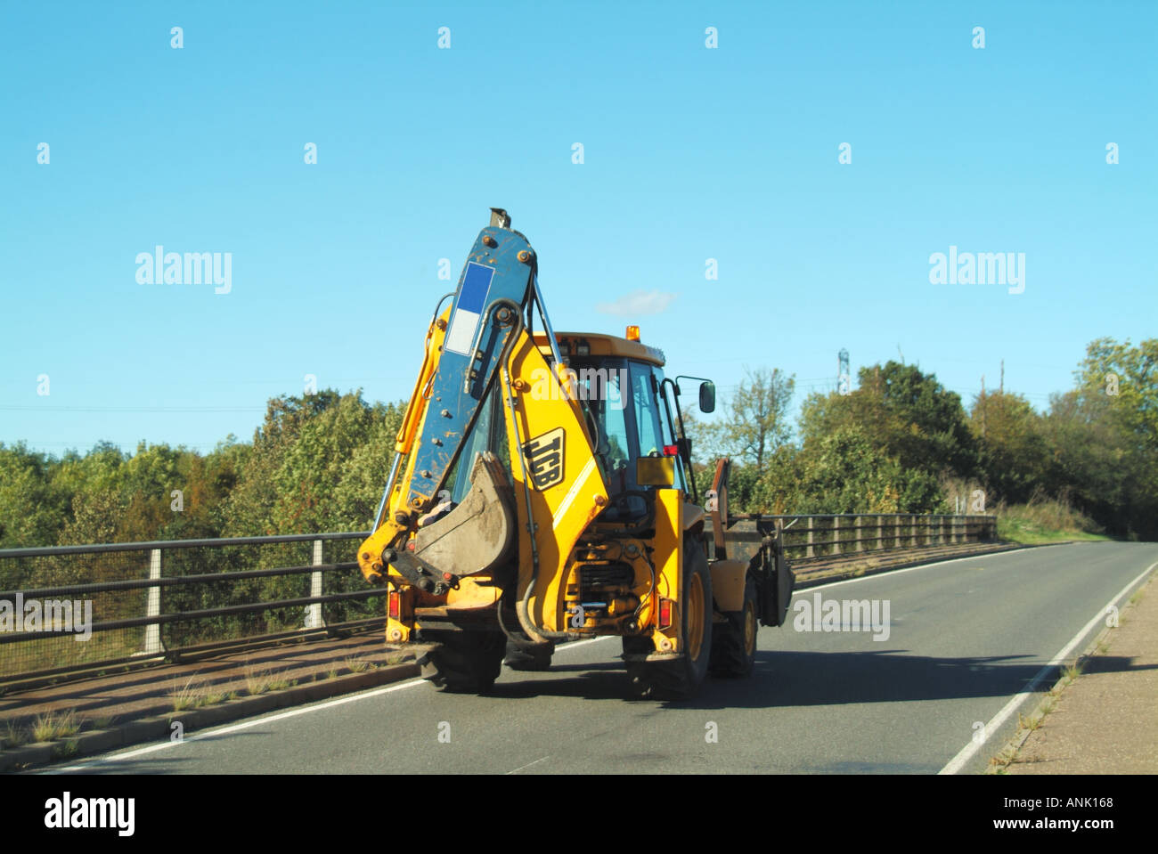 JCB hydraulic back actor excavator being driven along country road bridge hire company name digitally removed Stock Photo