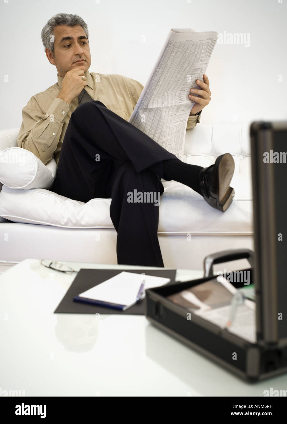 Businessman sitting on a couch and reading a newspaper Stock Photo - Alamy
