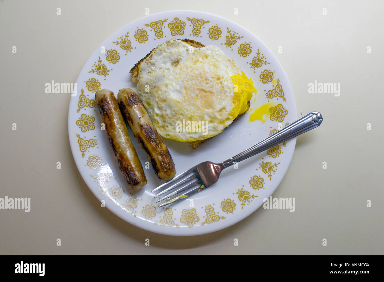 Overeasy egg and sausage links on a white plate with a fork Stock Photo