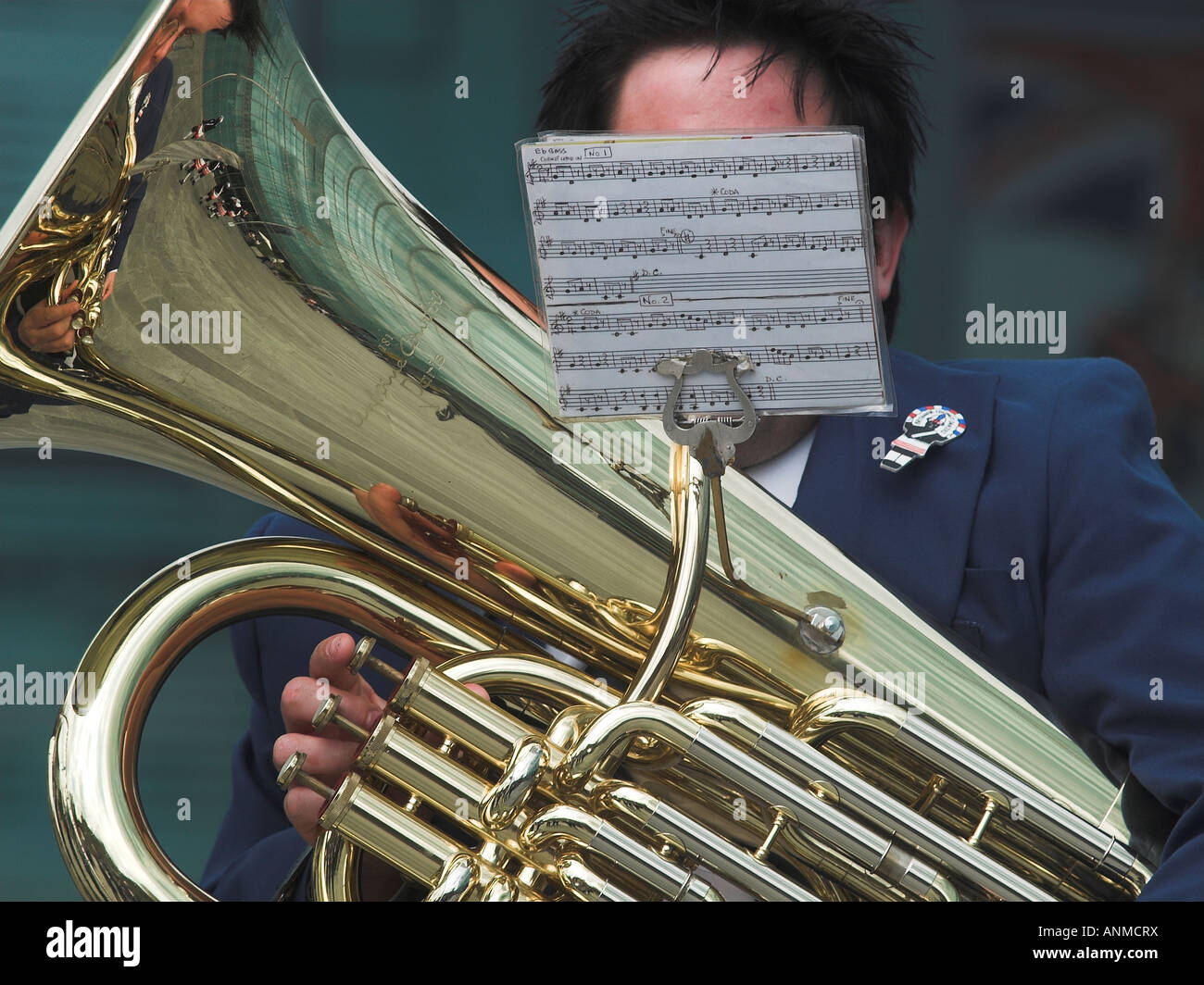 Tuba player player in brass band. Player and buildings are reflected in the polished tuba. Face not visible. Stock Photo