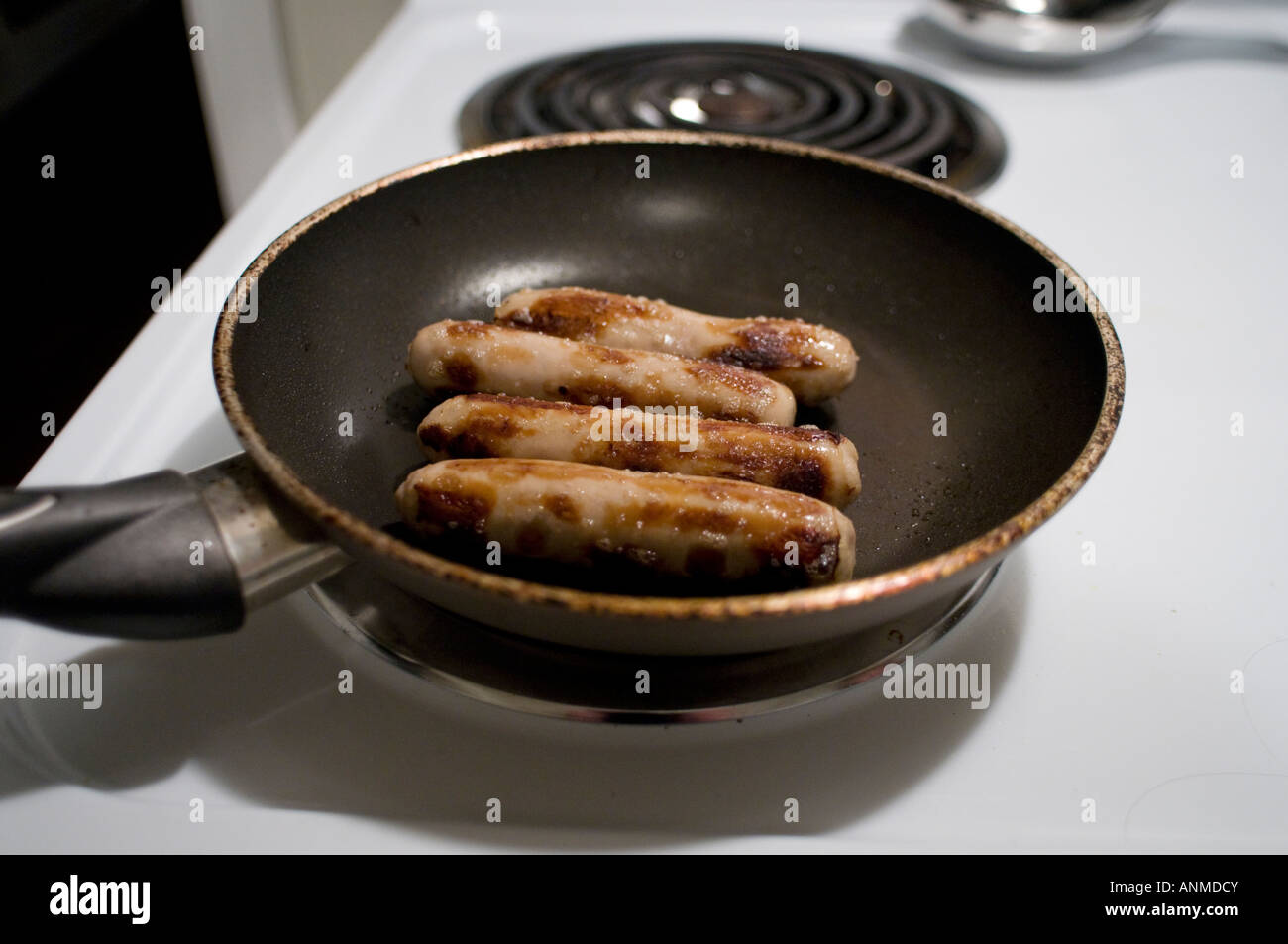 Four sausage links in a frying pan on a white stove Stock Photo