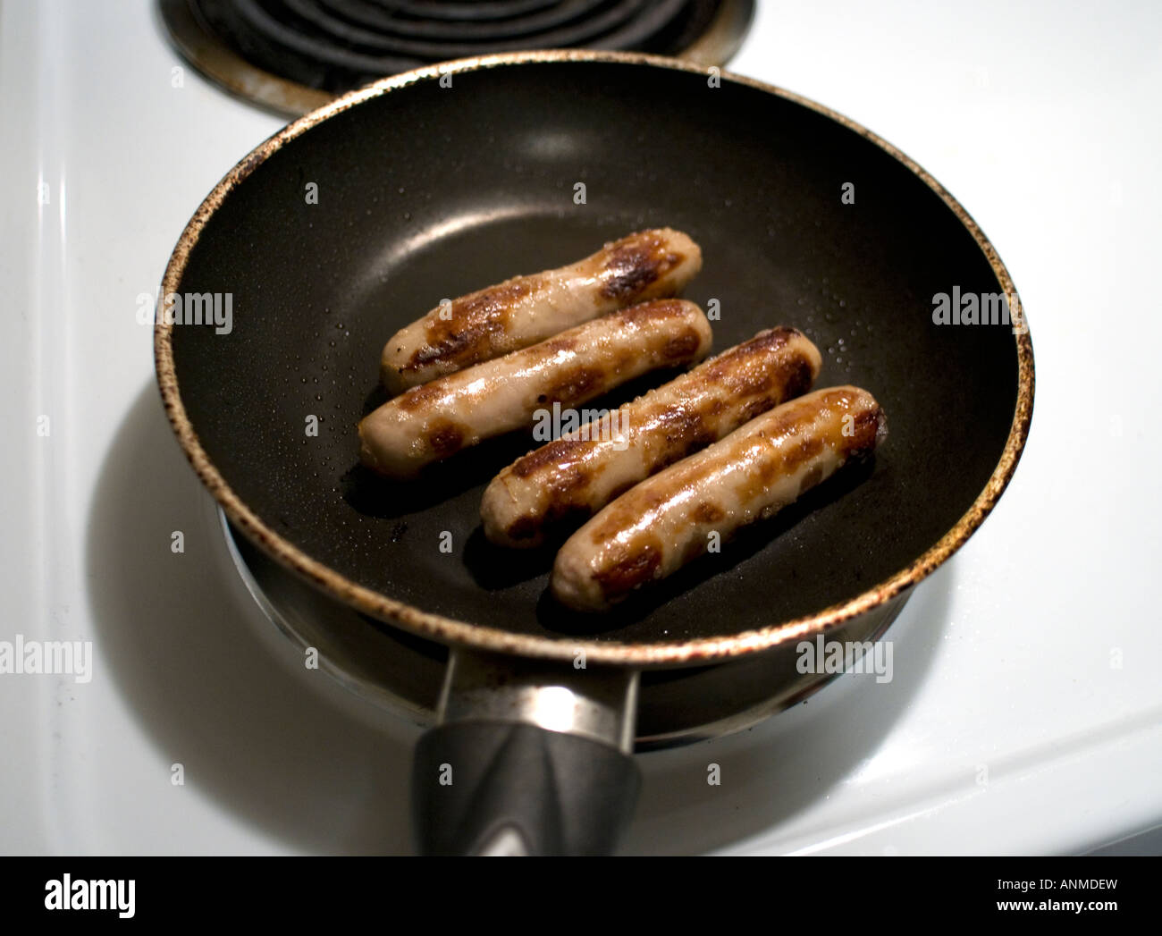 Four sausage links in a frying pan on a white stove Stock Photo