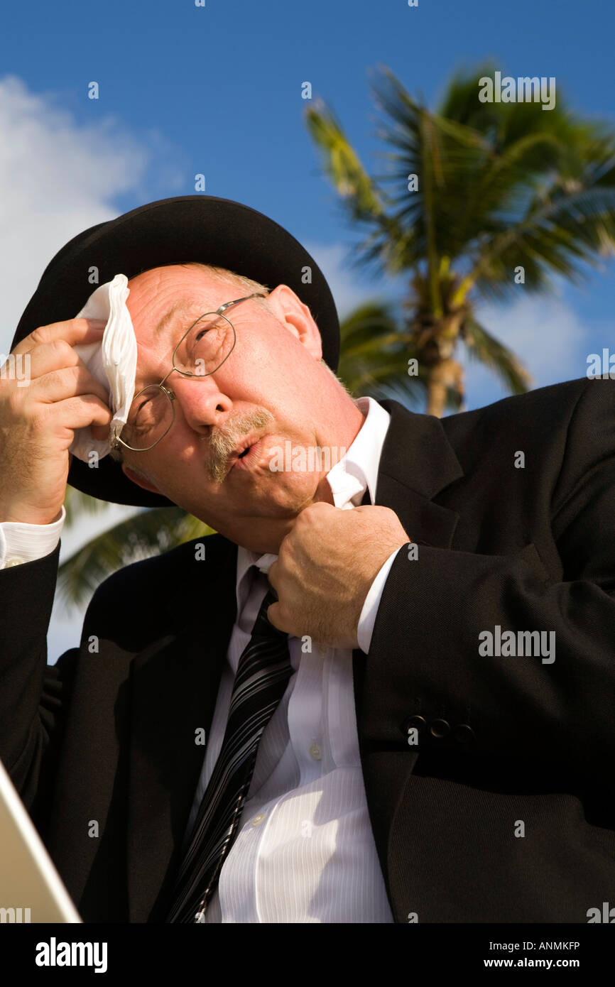 Maldives hot sweaty businessman in bowler hat and business suit on tropical beach Stock Photo