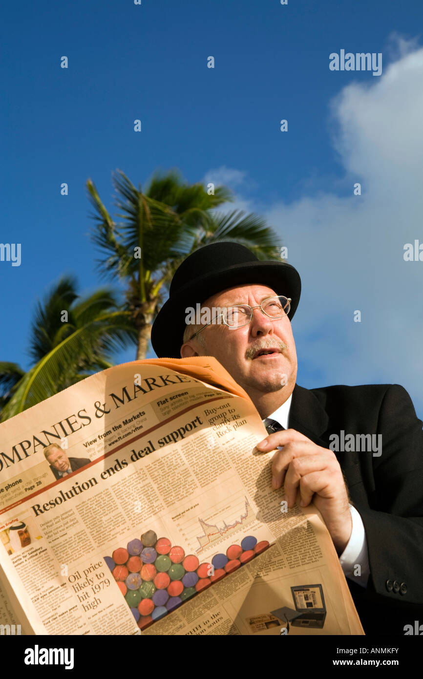 Maldives workaholic businessman in bowler hat reading financial newspaper under palm tree Stock Photo
