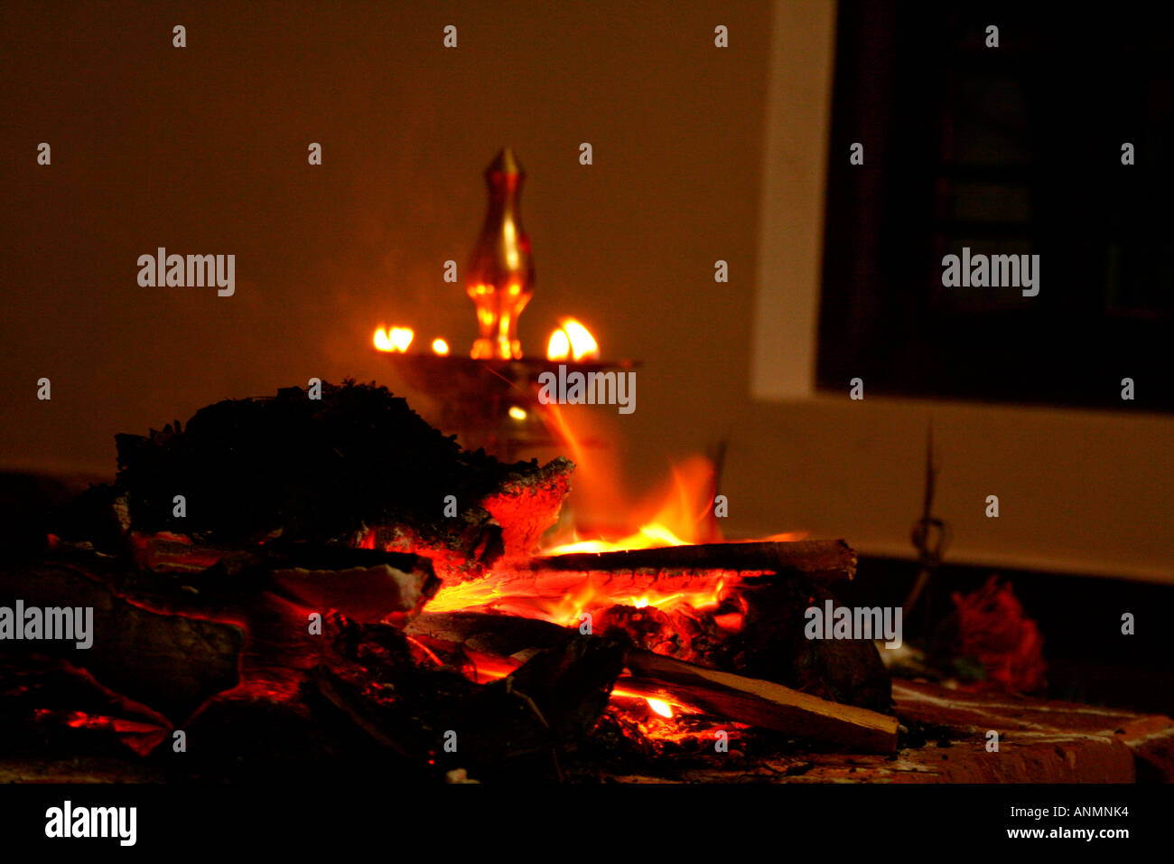 Dying flames in a sacrificial pit and a burning traditional Kerala style lamp beside Stock Photo
