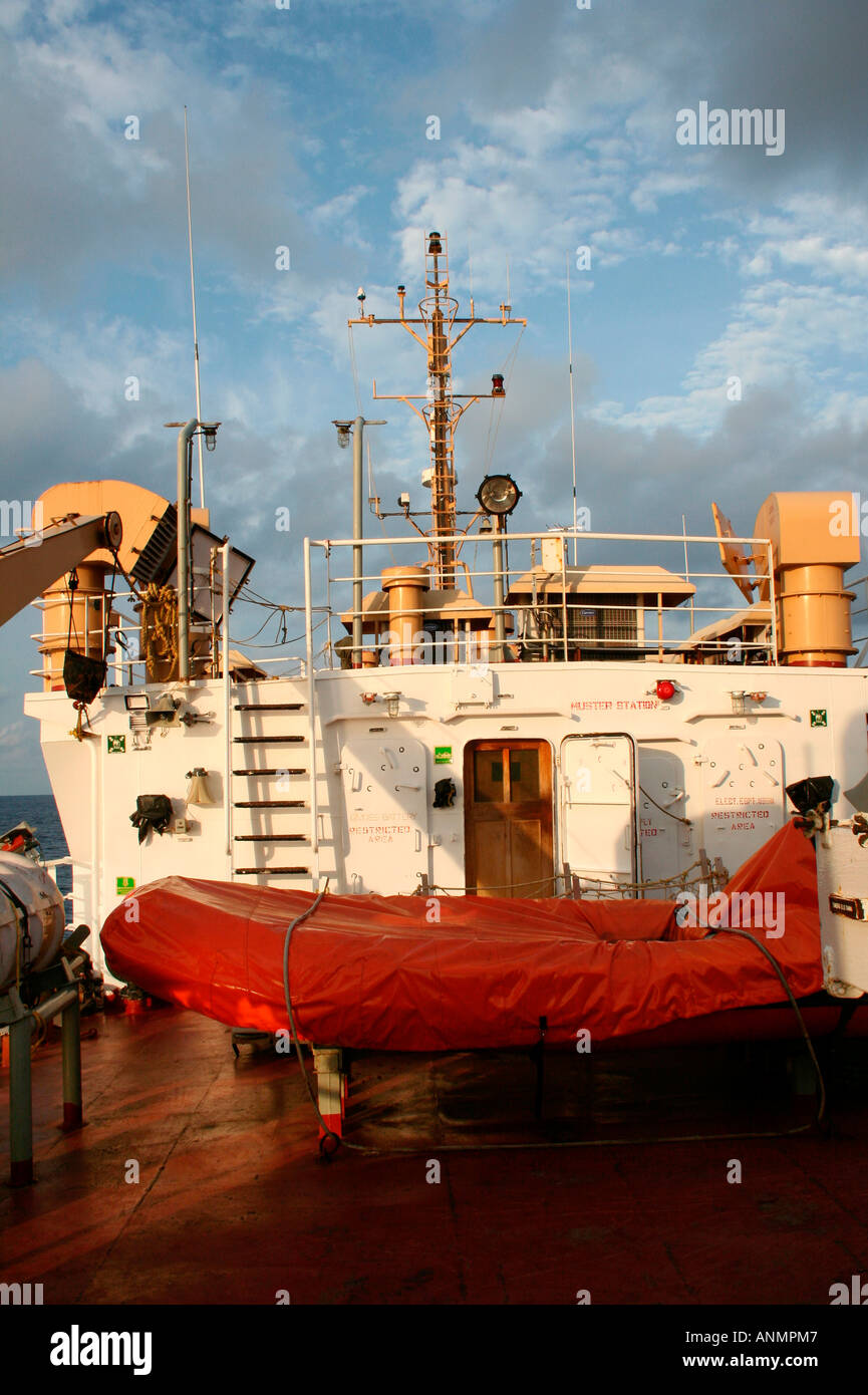 A covered lifeboat and other machinery on board a ship headed towards the Andaman with a view of the clouded blue sky Stock Photo