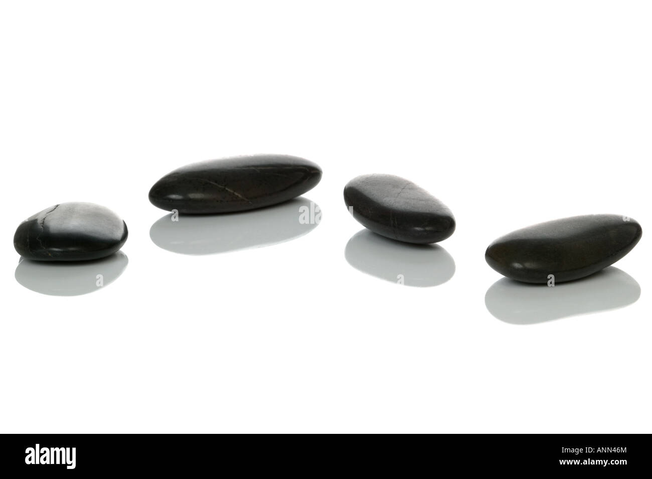 Four black pebbles with reflections on a white surface Stock Photo