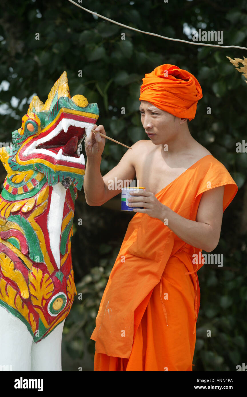 Monk in saffron robes painting a dragon statue in colourful red yellow ...