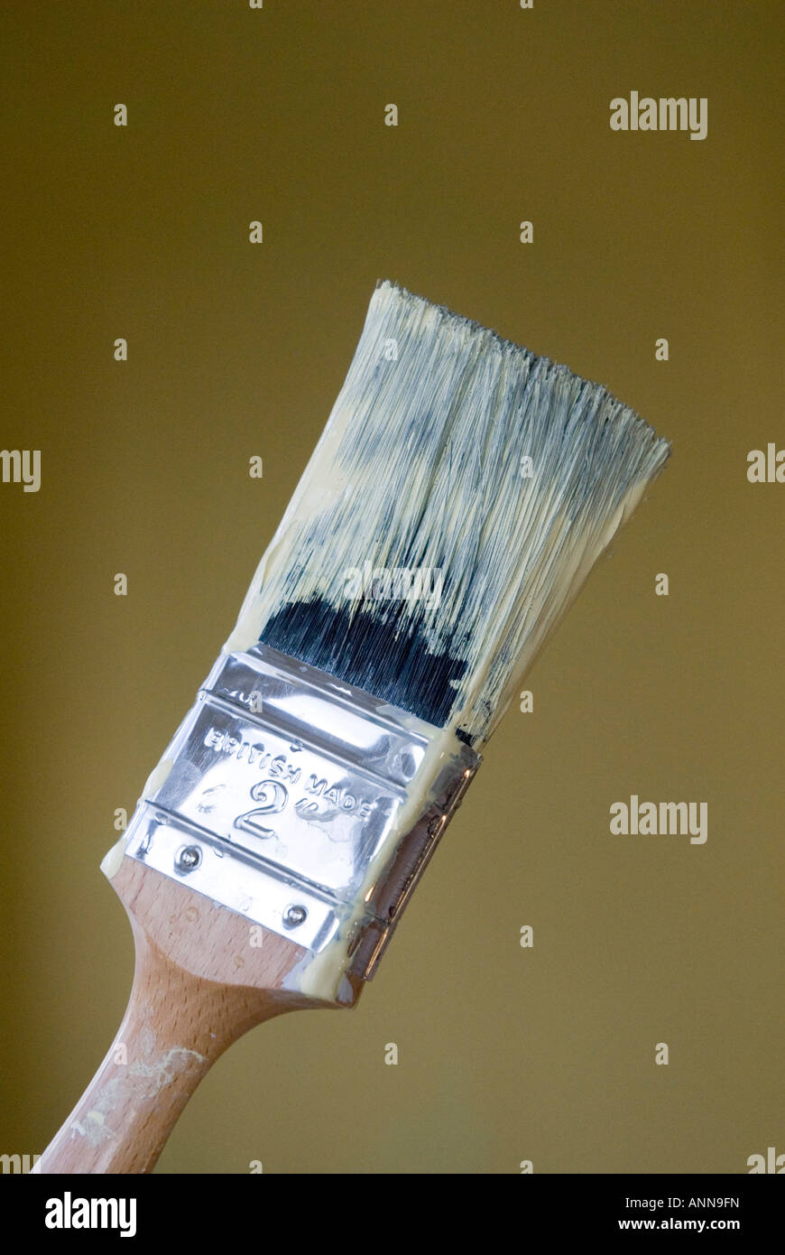 close up of paint brush with yellow paint upright plain background