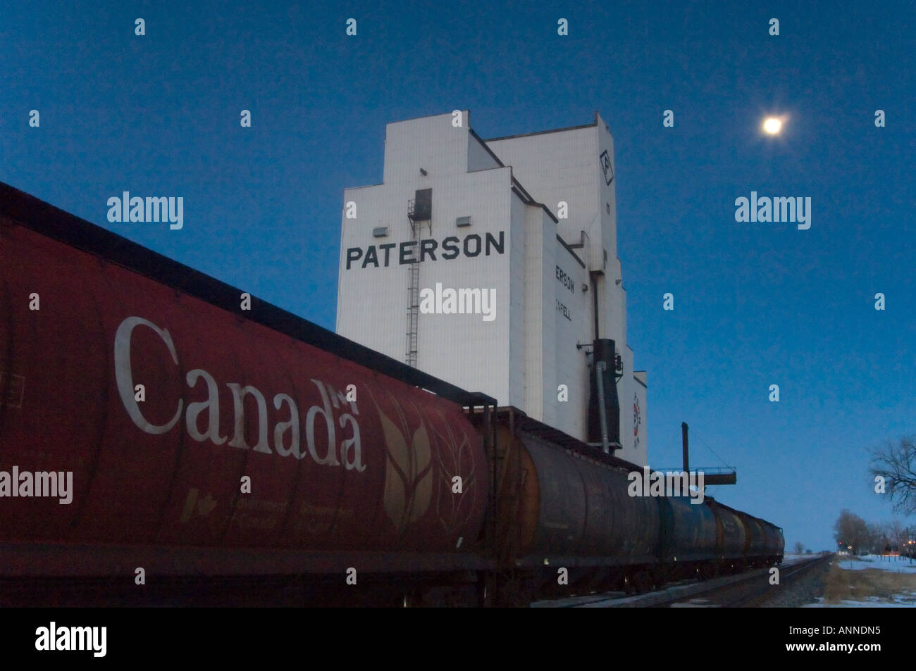 Grain elevator, rail cars and full moon at dusk, Whitewood, Saskatchewan, Canada Stock Photo