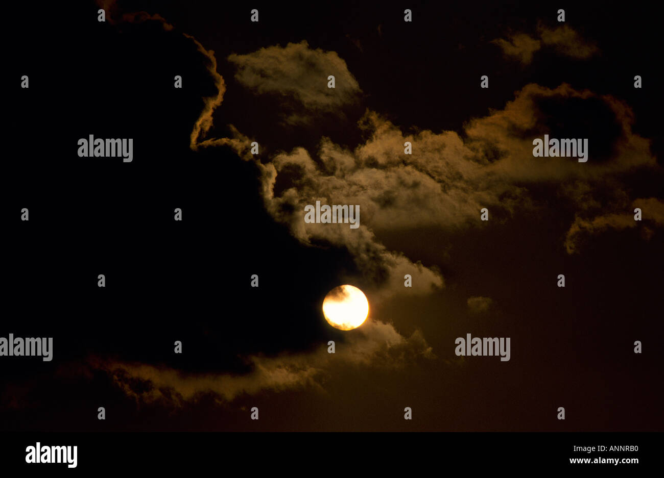 Moon edging through dark cloud with rim lighting and diffused wisps in ...