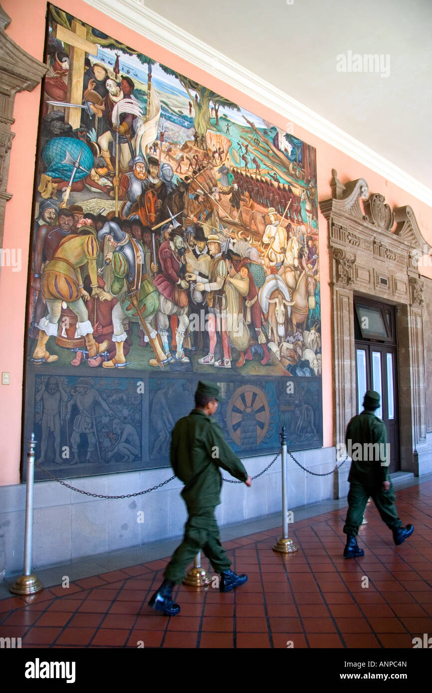 Men in military uniform walk past a mural painted by Diego Rivera at the National Palace in Mexico City Mexico Stock Photo