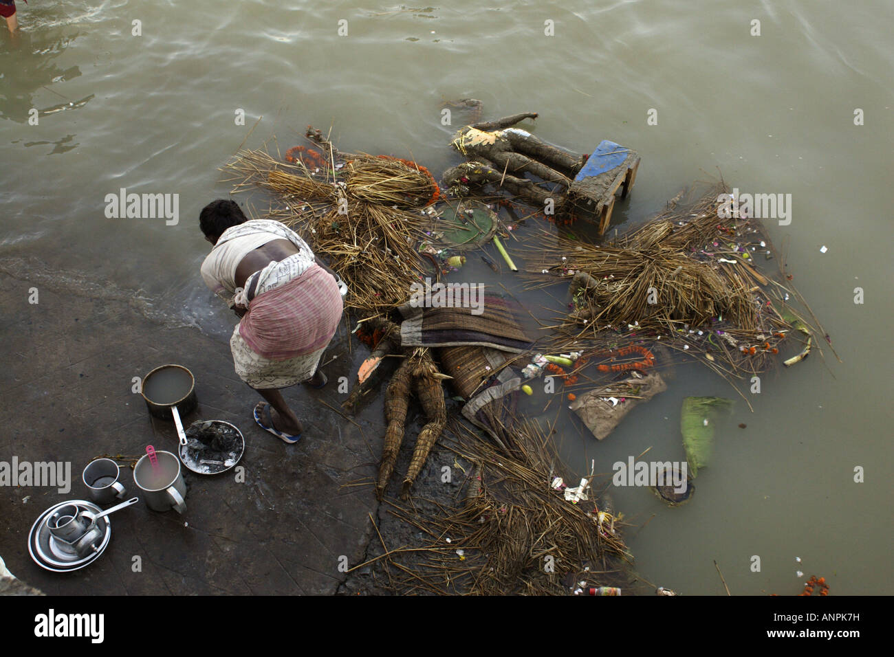 A woman washes her cooking utensils in the Hooghly River, in Kolkata, India. Waste floats in the river next to her. Stock Photo