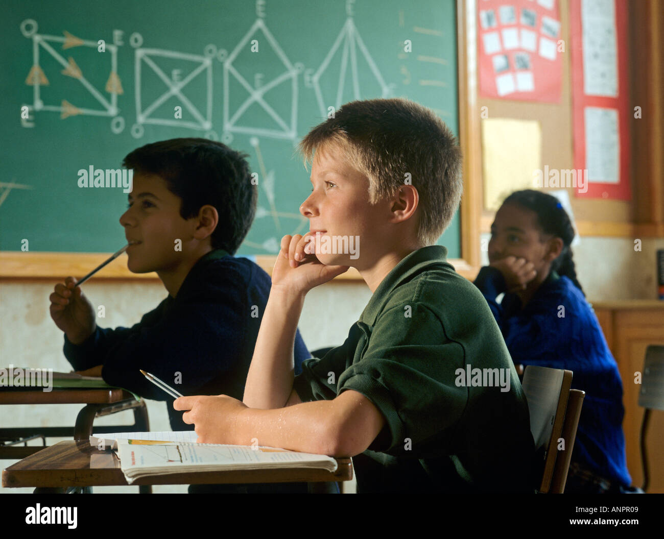 Boy (11-12) at desk,resting on elbow, geometry diagrams on wall behind Stock Photo