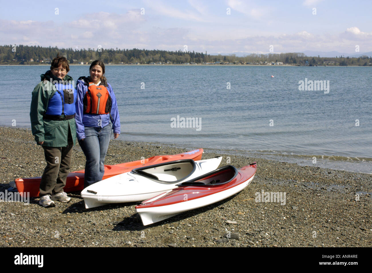 Washington San Juan Islands Smiling women stand near their sea kayaks ready to go paddling on Lummi Island Stock Photo