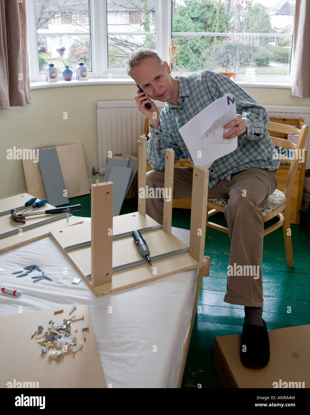 man at home in difficulty constructing flat pack furniture calling for