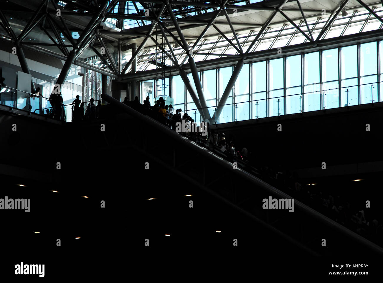 An escalator carrying people descends into darkness. Stock Photo