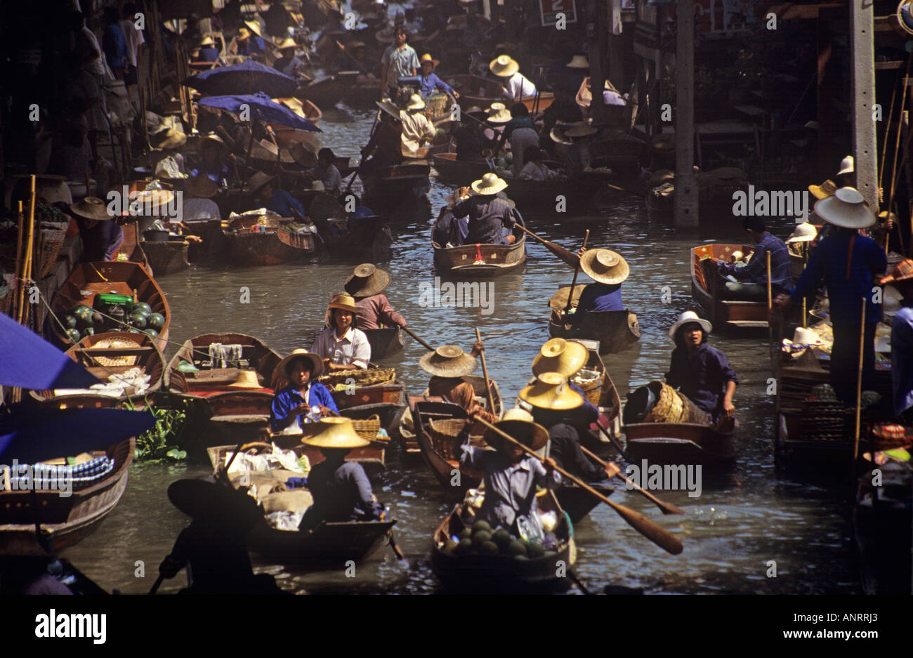 A large number of locals all wearing traditional wide brimmed hats in small wooden boats filled with fresh produce and other items to sell at the floating market at Damnoen Saduak Stock Photo