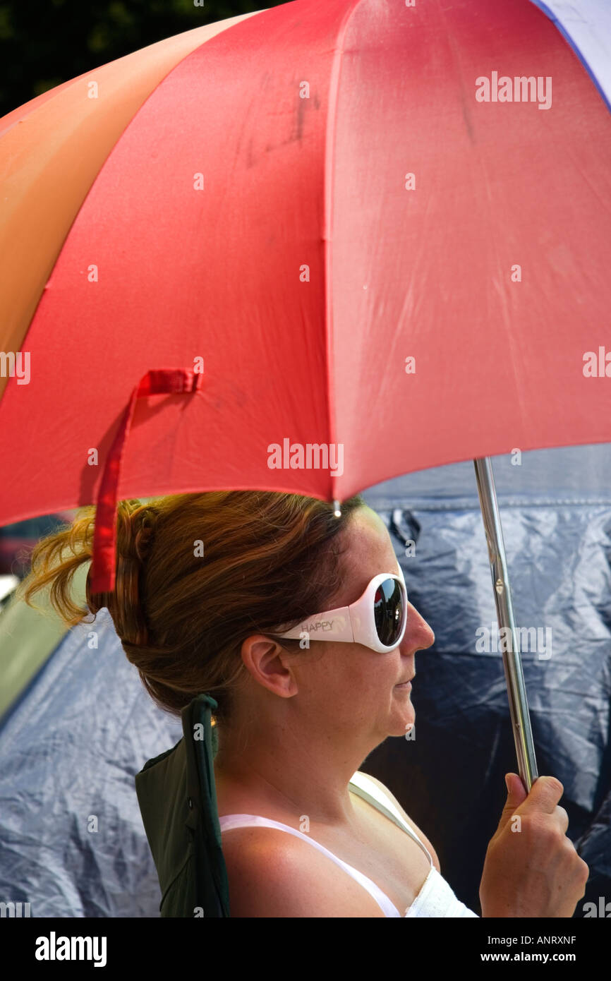 a woman wearing large white sunglasses holding very colourful umbrella to protect her from the hot summer sunshine Stock Photo