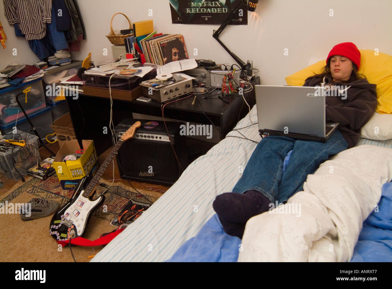 A teenage boy using a lap top in his untidy bedroom Stock Photo