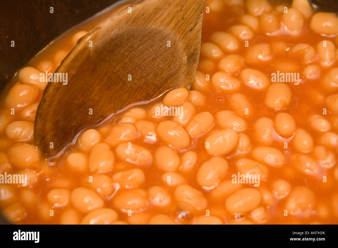 Baked  beans cooking in a saucepan, being stirred with a wooden spoon Stock Photo