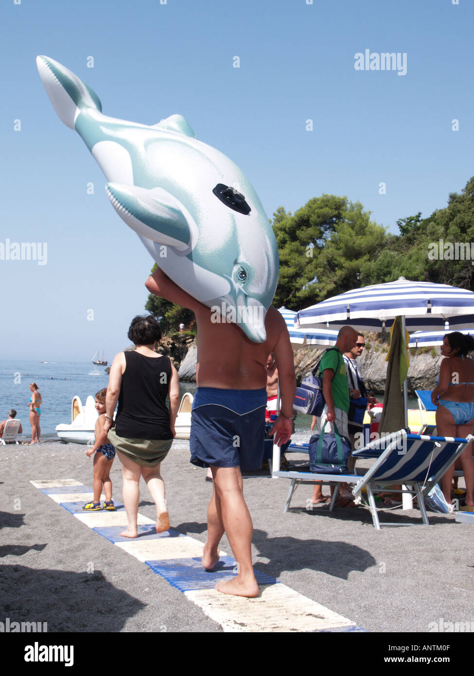 man walking on beach carrying inflatable blow up dolphin Stock Photo