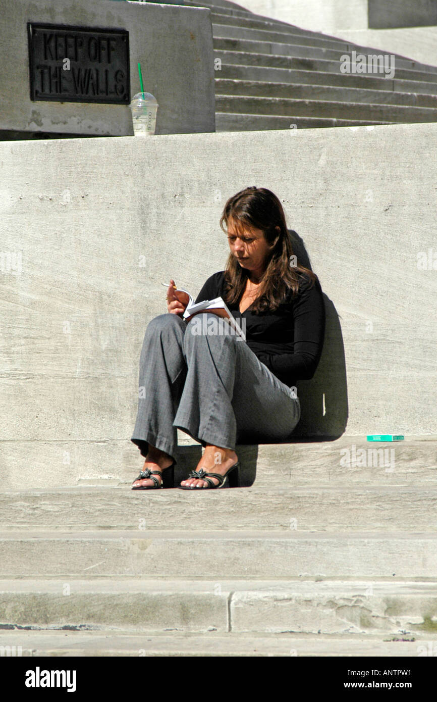 Adult Female smoking a cigarette and reading a book during her lunch break Stock Photo