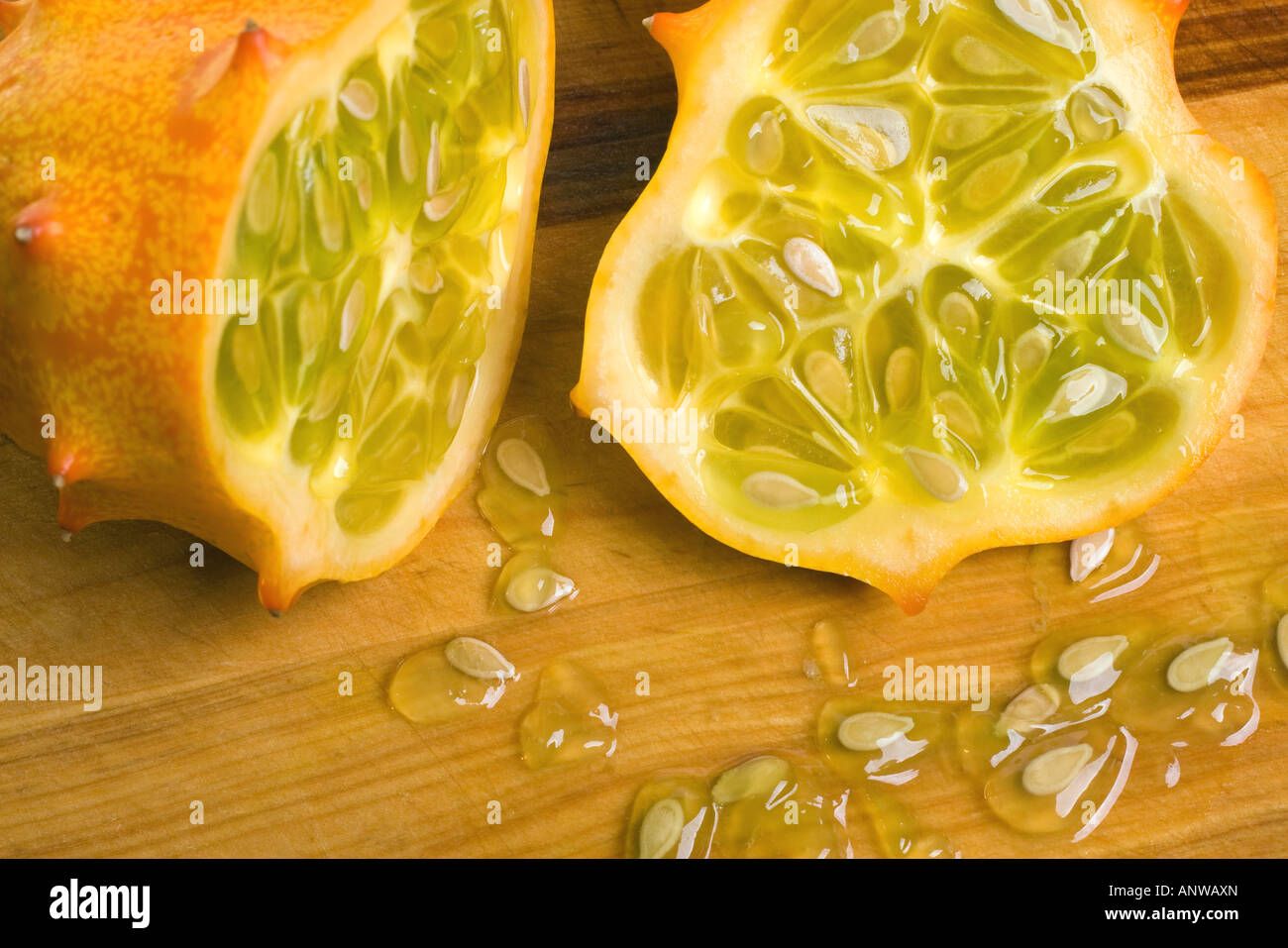 A juicy sliced open horned or Kiwano melon showing the seeds and yellow green flesh on cutting board Stock Photo