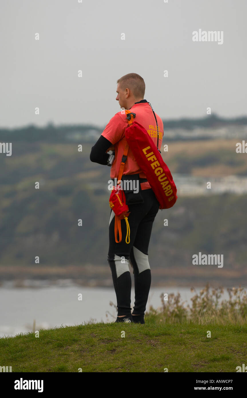 Lifeguard wearing a wetsuit standing alone watching the beach below
