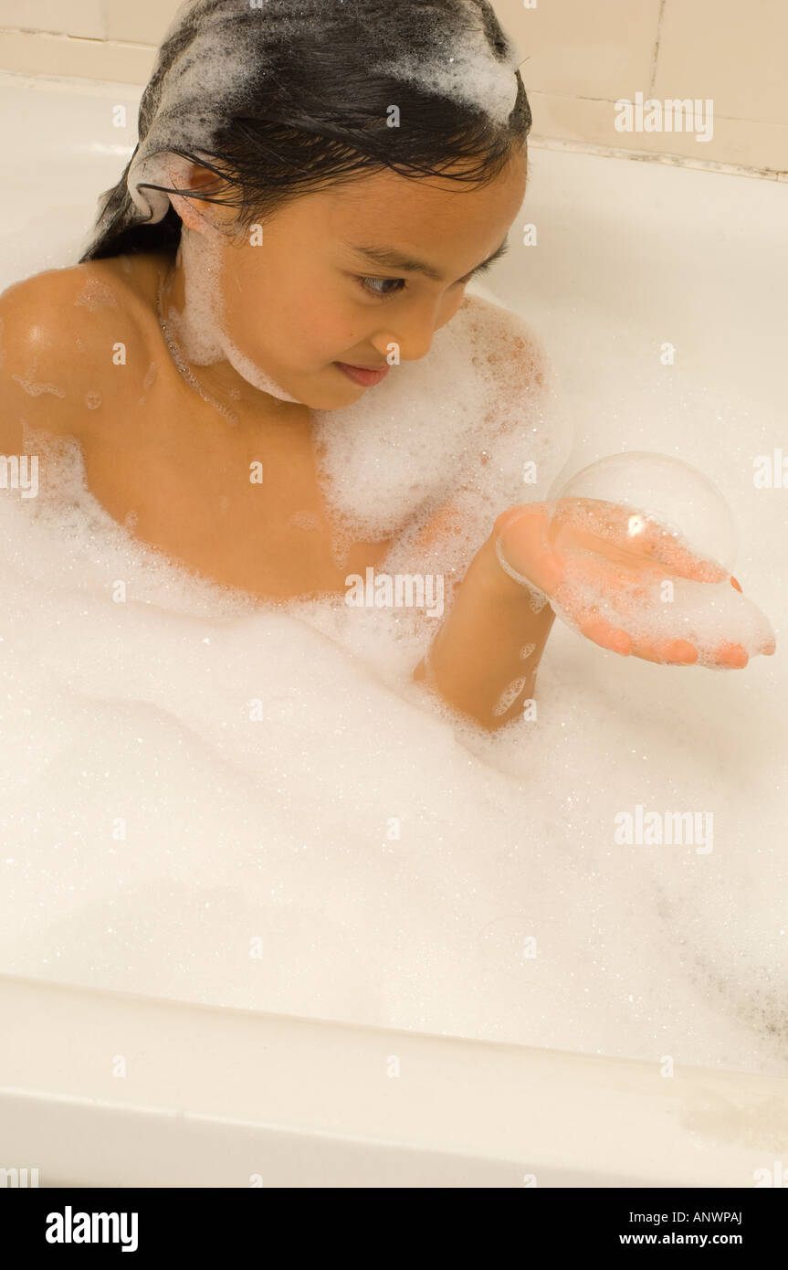 7 year old girl in bubble bath looking at soap bubbles on hand Asian