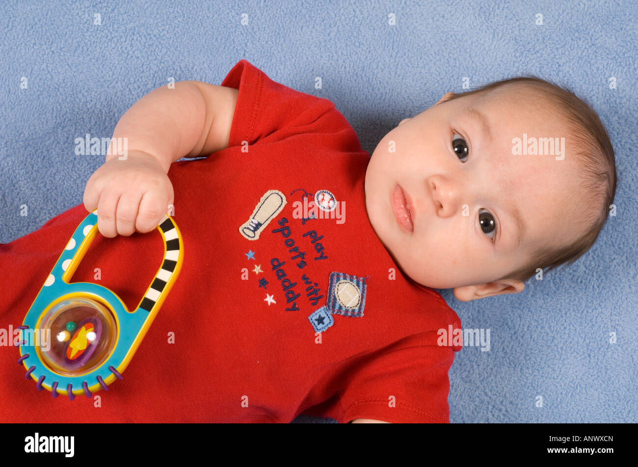 3 month old baby boy holding toy rattle in fist palmar grasp closeup on back, looking at viewer Stock Photo