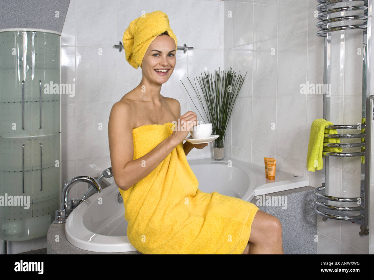 young woman in yellow towels sitting on the bath-tub with a cup of coffee Stock Photo