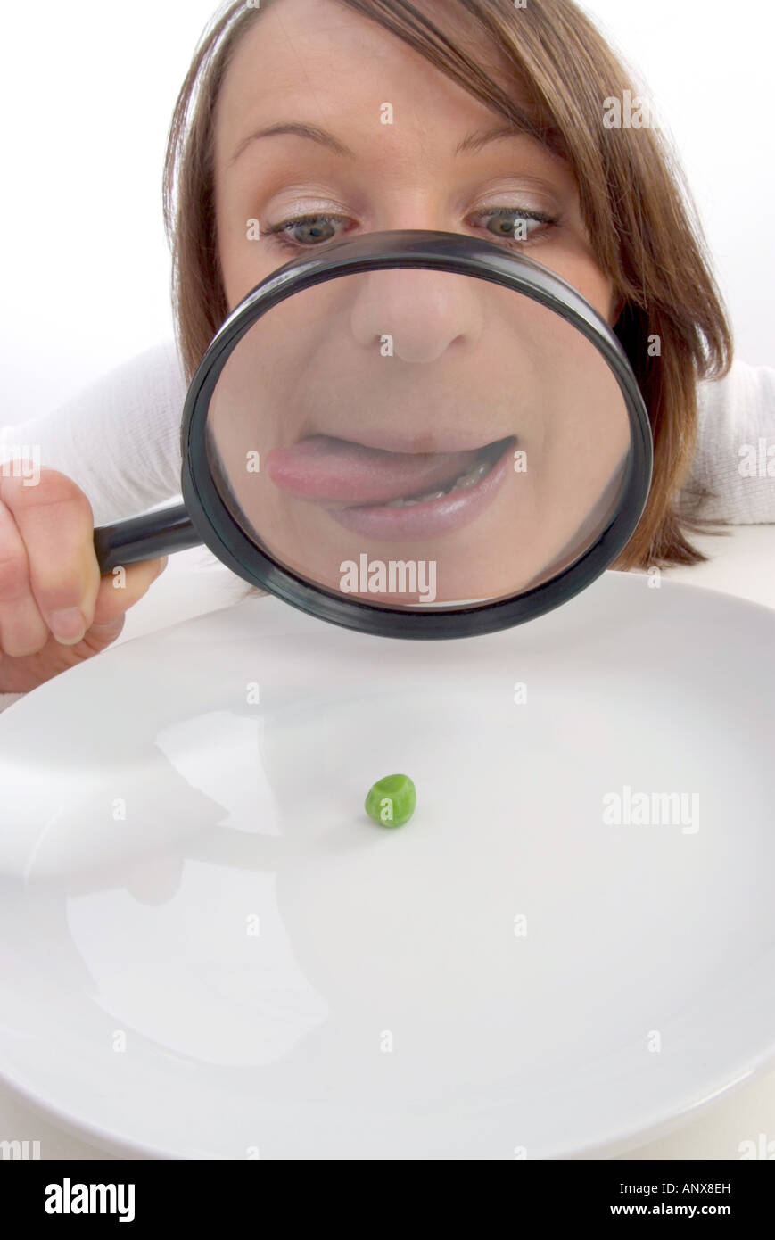 woman with magnifying glass viewed pea at plate Stock Photo