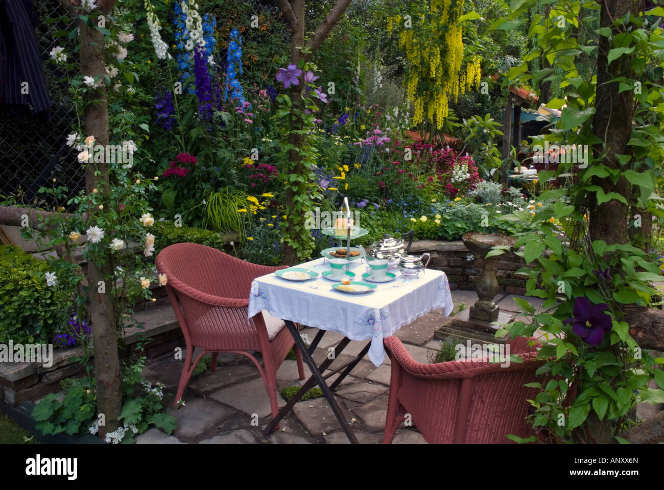 Lush garden set for eating tea or breakfast with chairs & table dining on the patio, filled with colorful flowers and plants Stock Photo