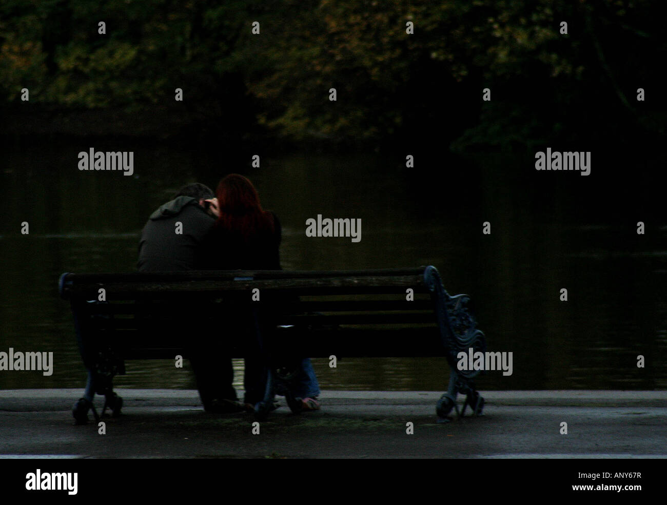 Couple Cuddling On Park Bench By Lake In Autmn Light Stock Photo