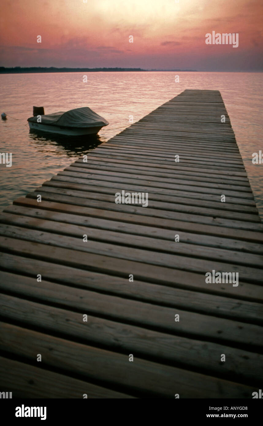 Small speedboat tethered to a wooden jetty with dramatic sunset on the water Stock Photo