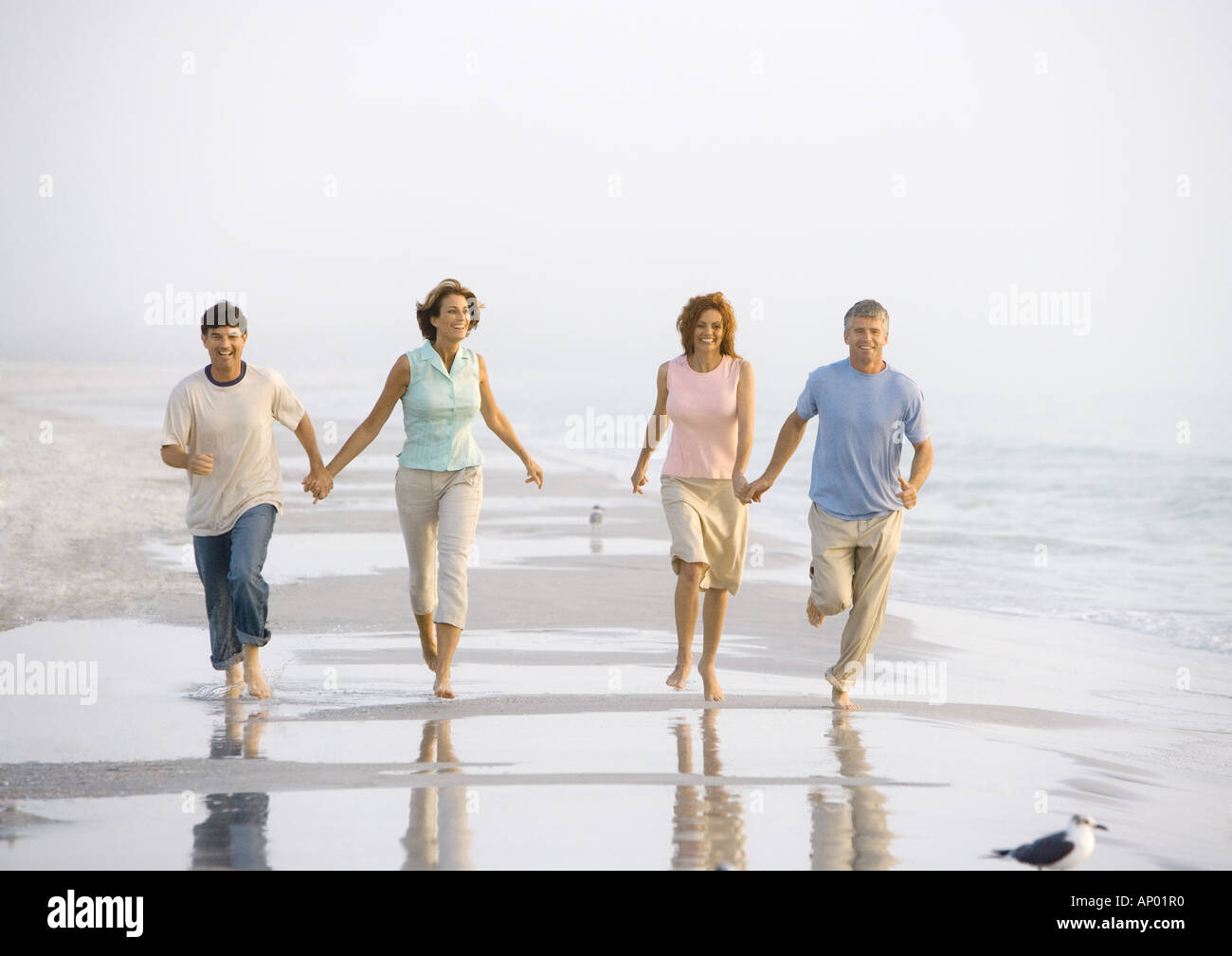 Two mature couples walking on beach, holding hands Stock Photo