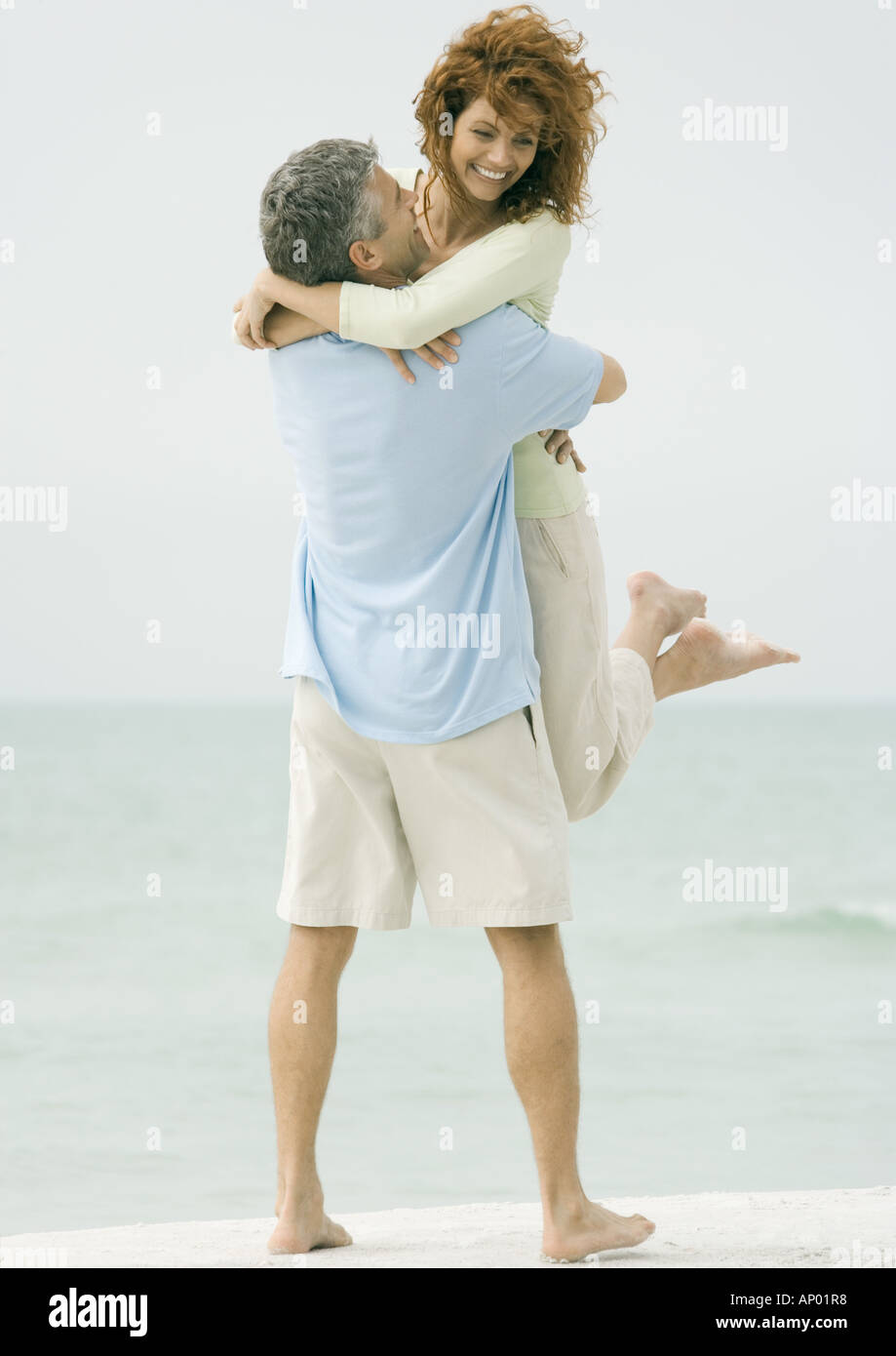Mature couple, man picking up woman on beach Stock Photo
