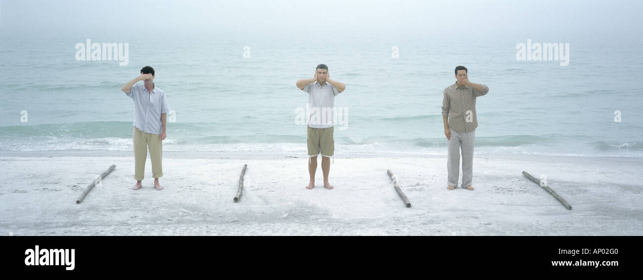 Three men performing hear no evil, speak no evil, see no evil, on beach Stock Photo