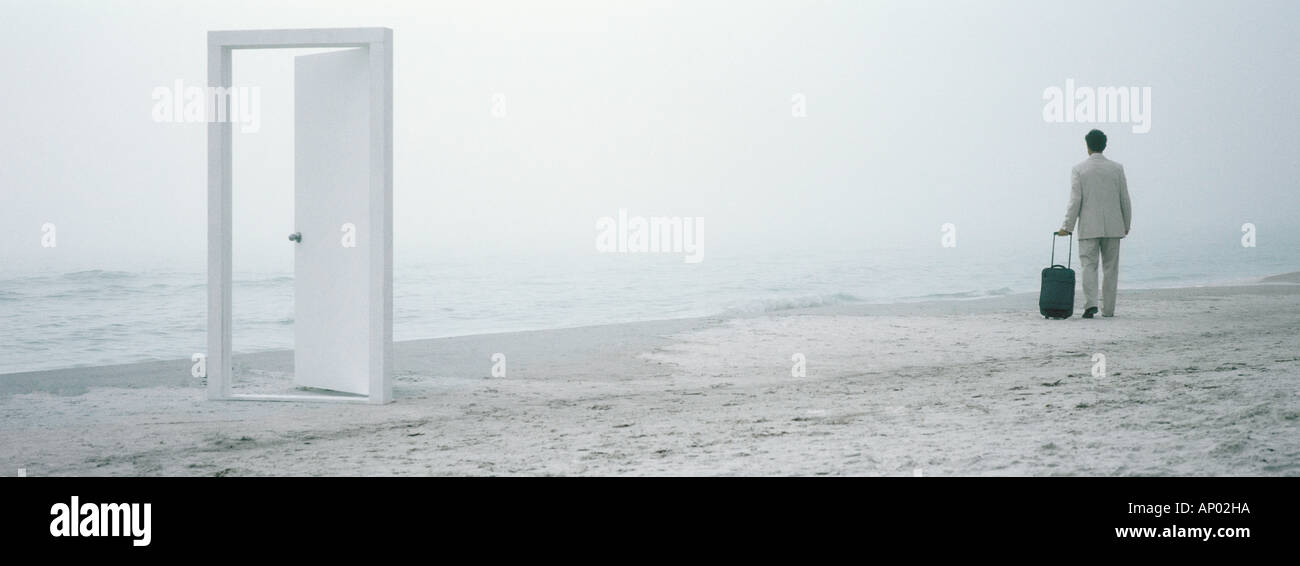 Man walking with suitcase on beach in mid-distance, doorframe in foreground Stock Photo