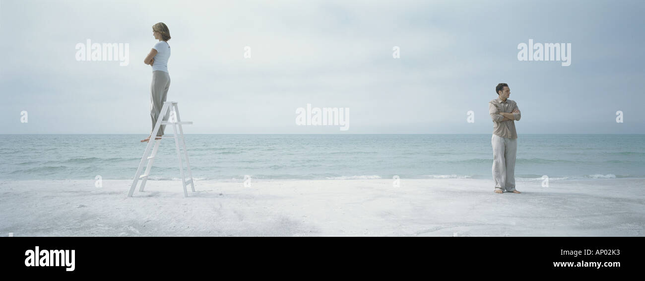 On beach, couple turning backs to each other, woman standing on stepladder Stock Photo