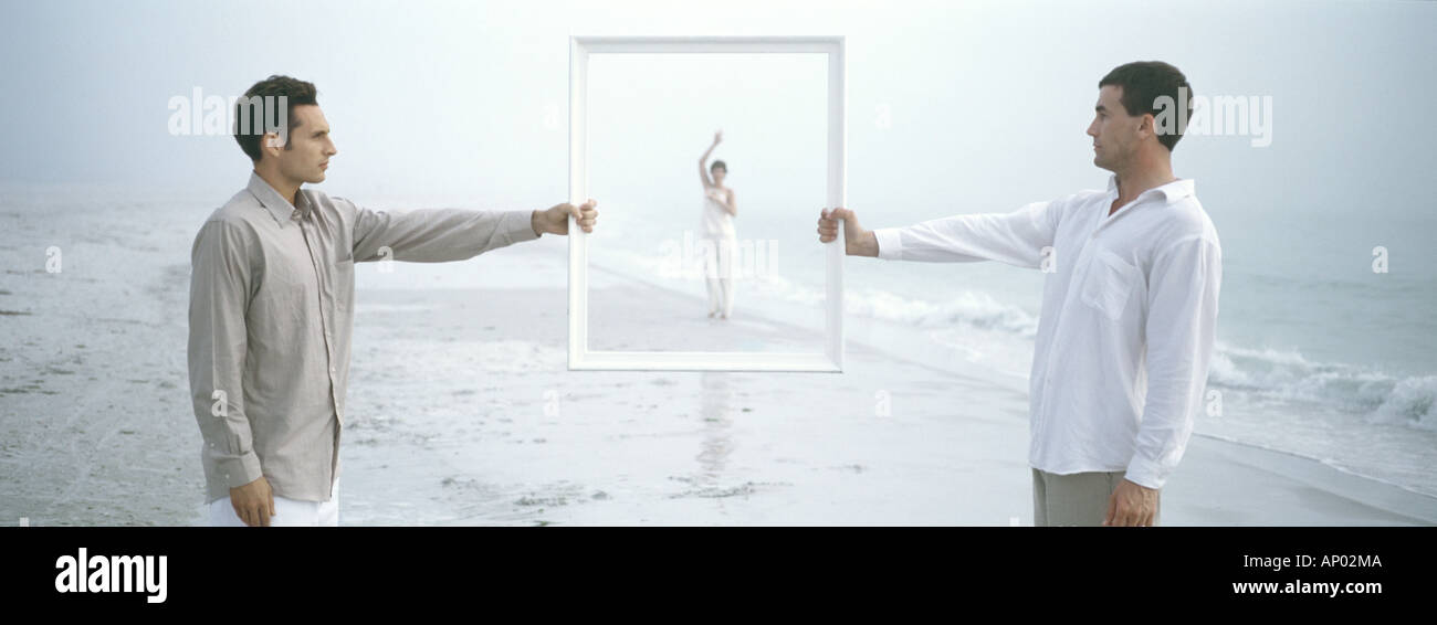 Two men holding frame, woman waving in frame in distance, on beach Stock Photo