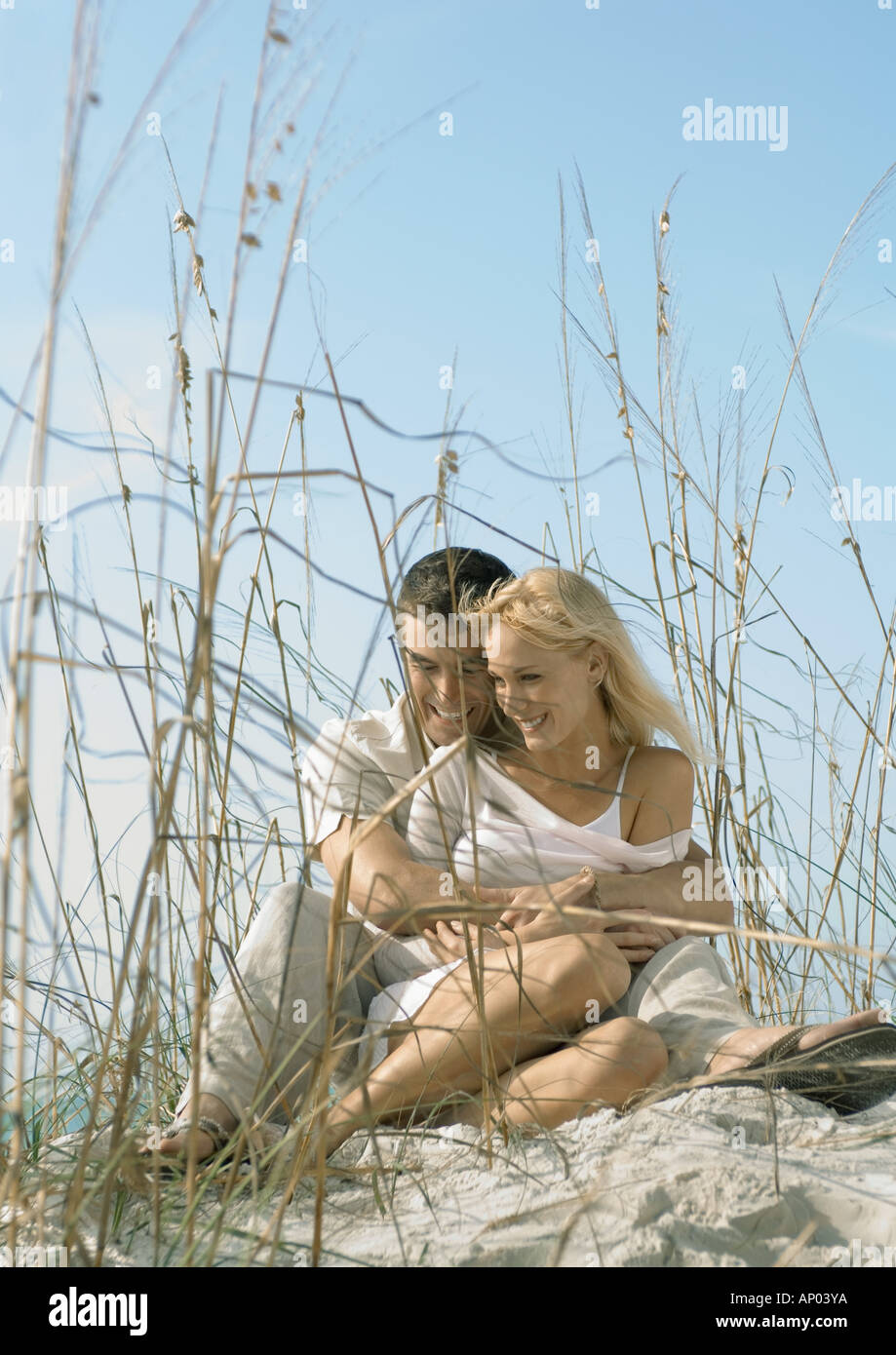 Couple sitting in dune grass, embracing Stock Photo