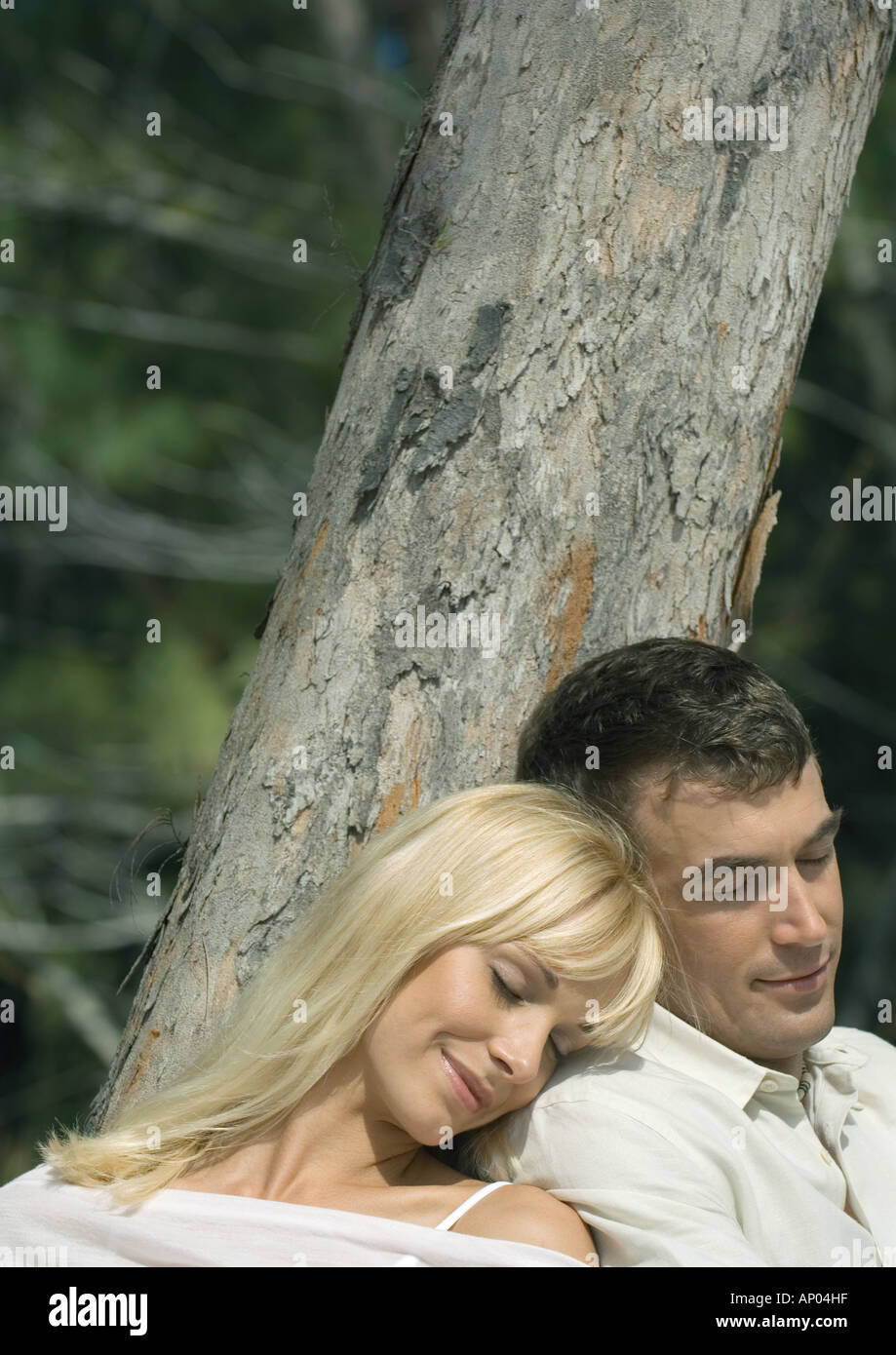 Couple leaning against tree, napping Stock Photo