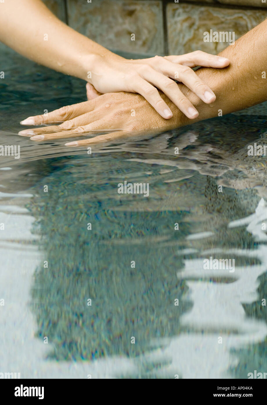 Woman's and man's hands on surface of pool water together Stock Photo