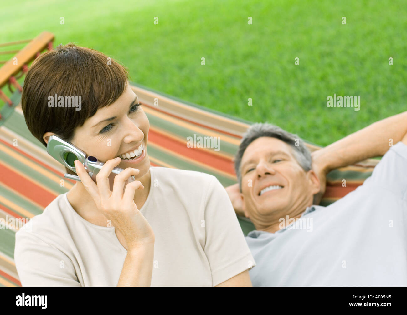 Woman using cell phone while man lounges on hammock Stock Photo