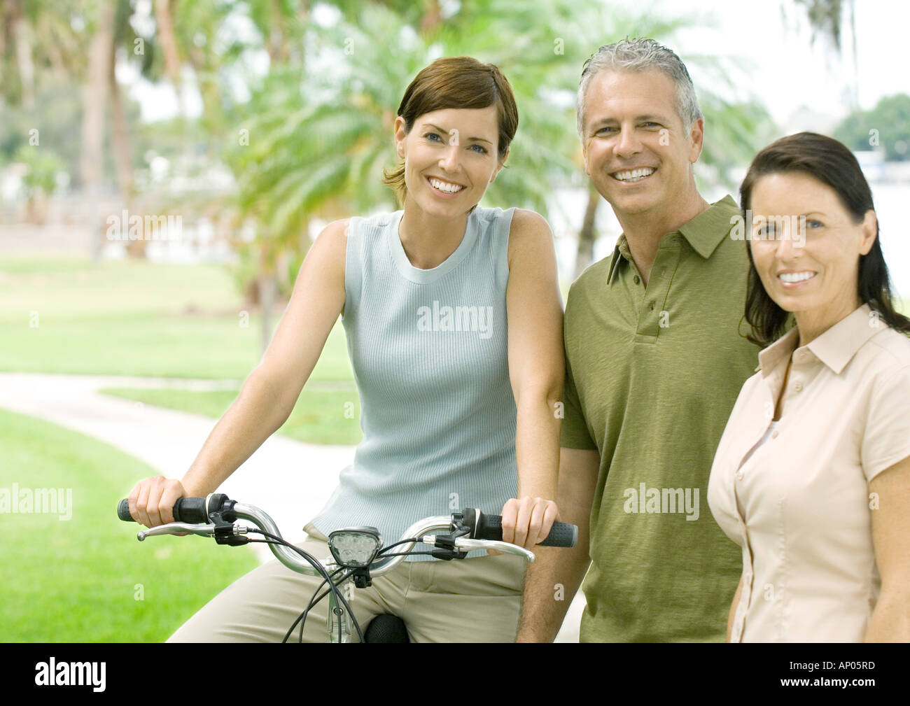 Three adult friends smiling at camera, one on bike Stock Photo
